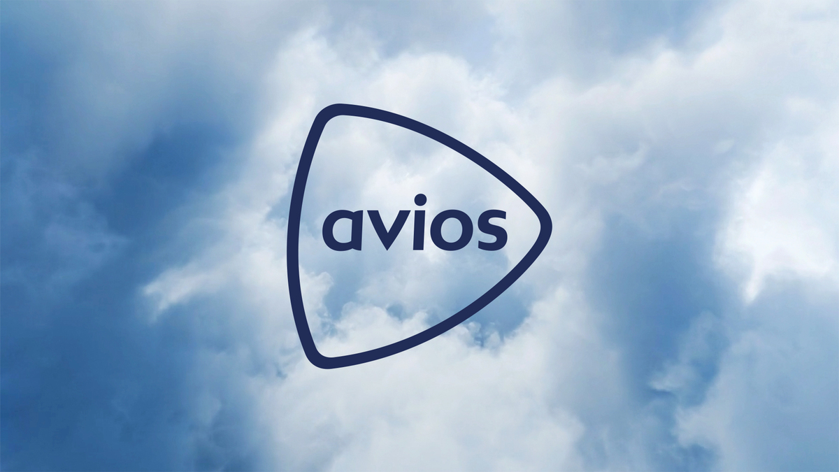 The official Avios logo in dark blue on a cloudy sky background, featuring the word "avios" inside a stylized triangular play-button-like shape.