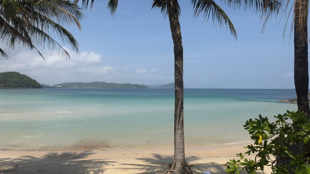 Premier Village Phu Quoc beach afternoon view with palm trees, turquoise bay, distant green hills and calm sea, Phu Quoc Vietnam resort