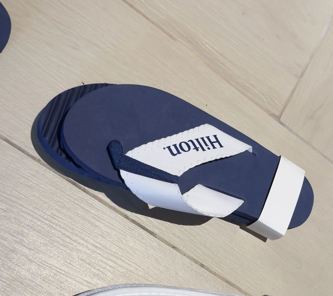 Navy Hilton branded flip-flops and white room slippers on a wooden floor