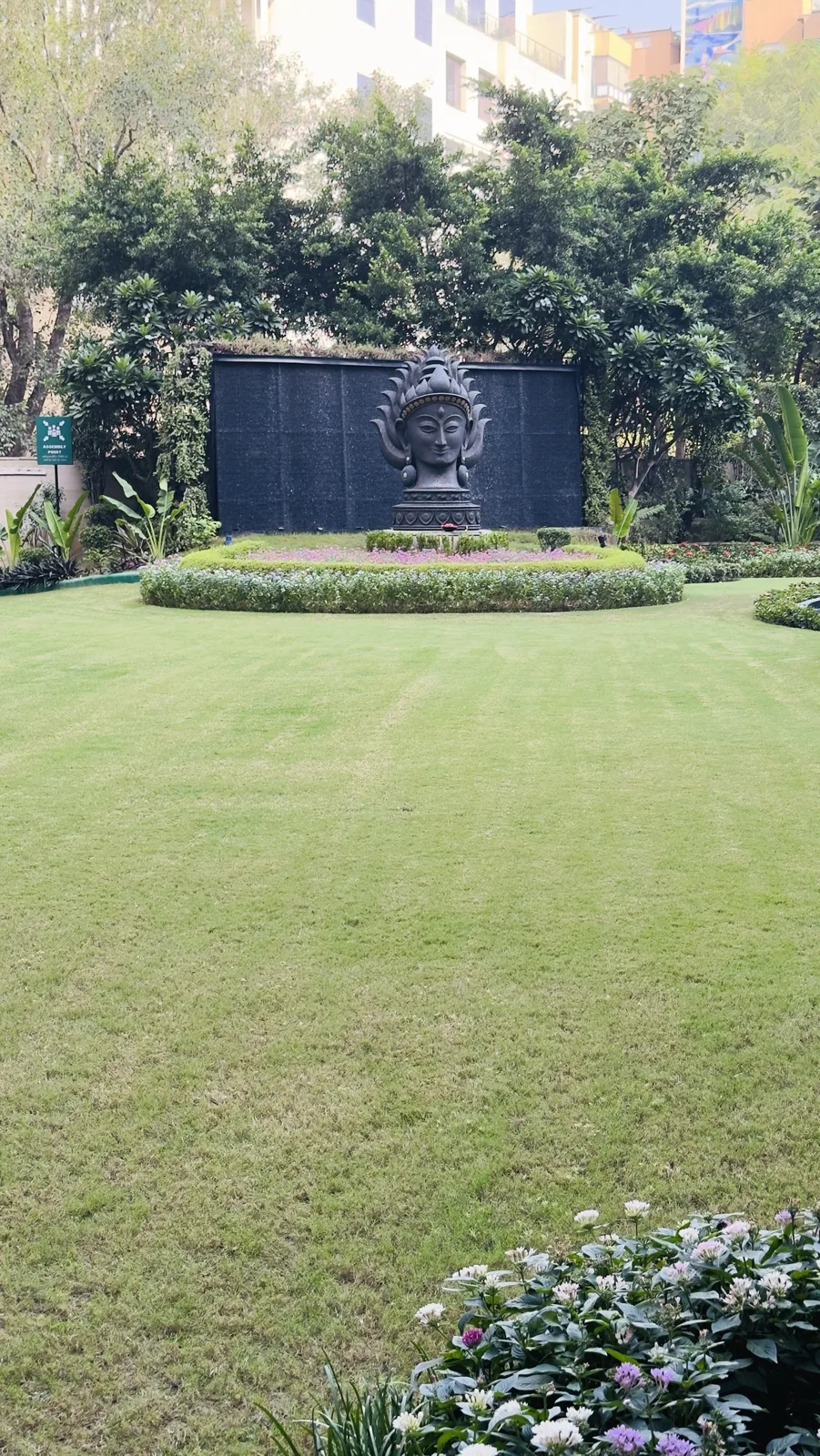 Manicured lawn with a large stone sculpture and water wall beside The Qube restaurant at The Leela Palace New Delhi